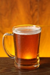 Mug with fresh beer on wooden table against color background