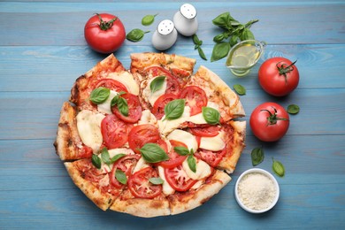 Photo of Delicious Caprese pizza and ingredients on blue wooden table, flat lay