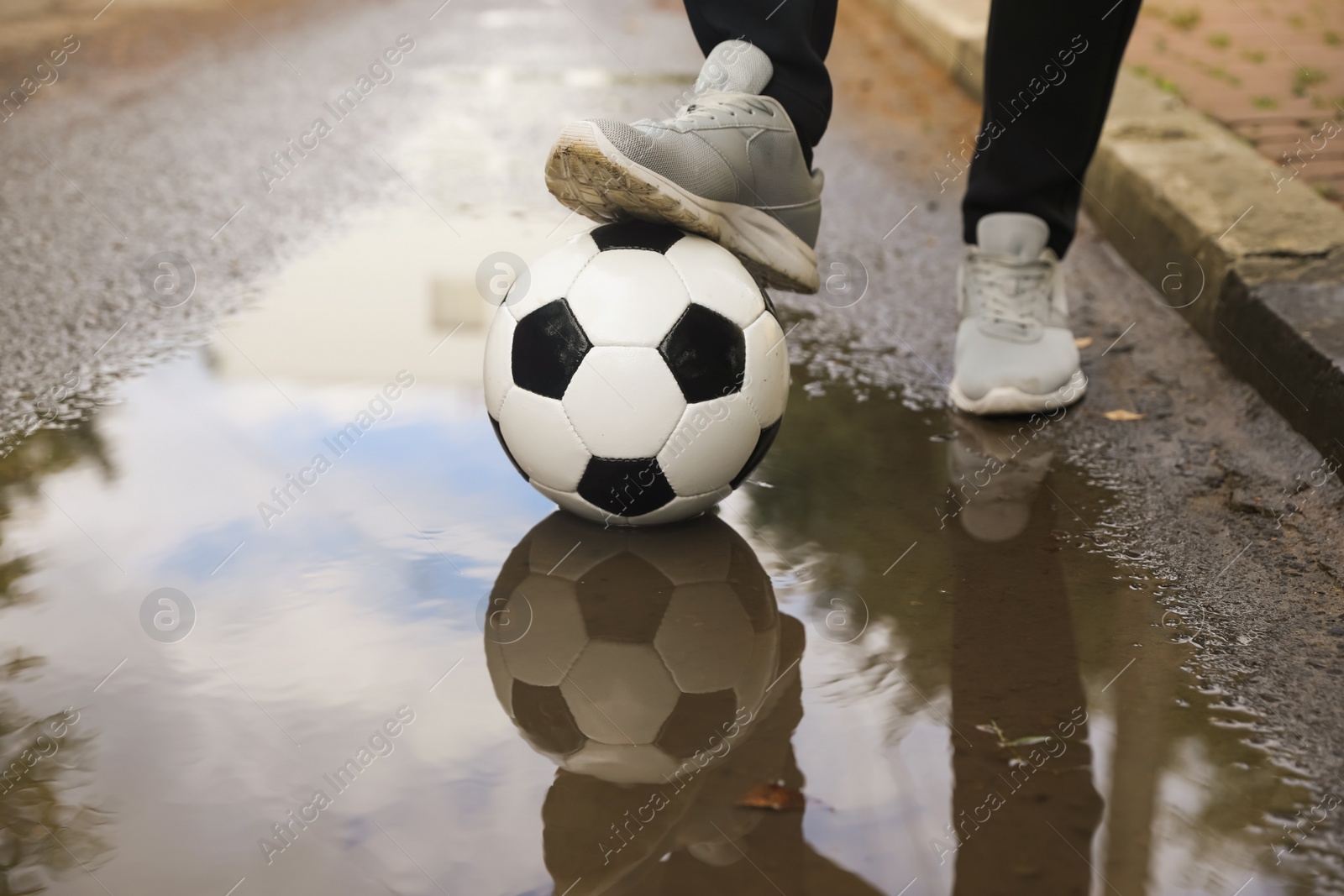 Photo of Man with soccer ball near puddle outdoors, closeup