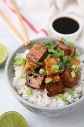 Photo of Bowl of rice with fried tofu and greens on white tiled table, closeup