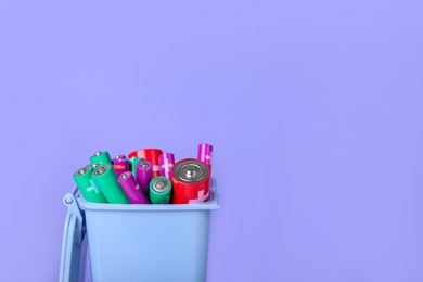 Many used batteries in recycling bin on light purple background. Space for text