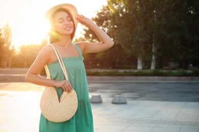 Photo of Young woman with stylish straw bag outdoors. Space for text