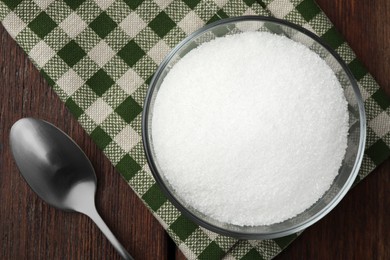 Photo of Granulated sugar in bowl, spoon and napkin on wooden table, top view