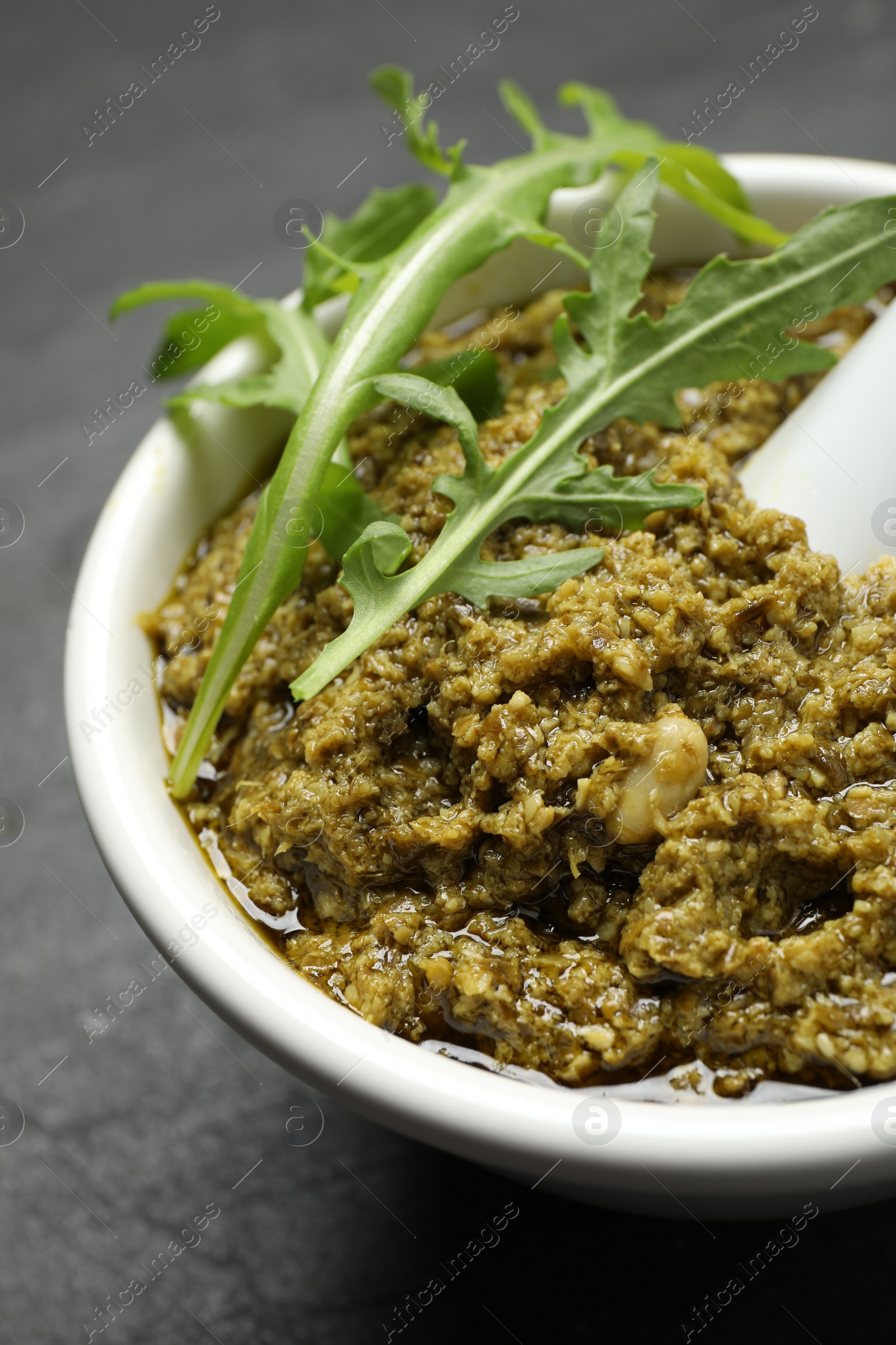 Photo of Mortar with tasty arugula pesto on black table, closeup