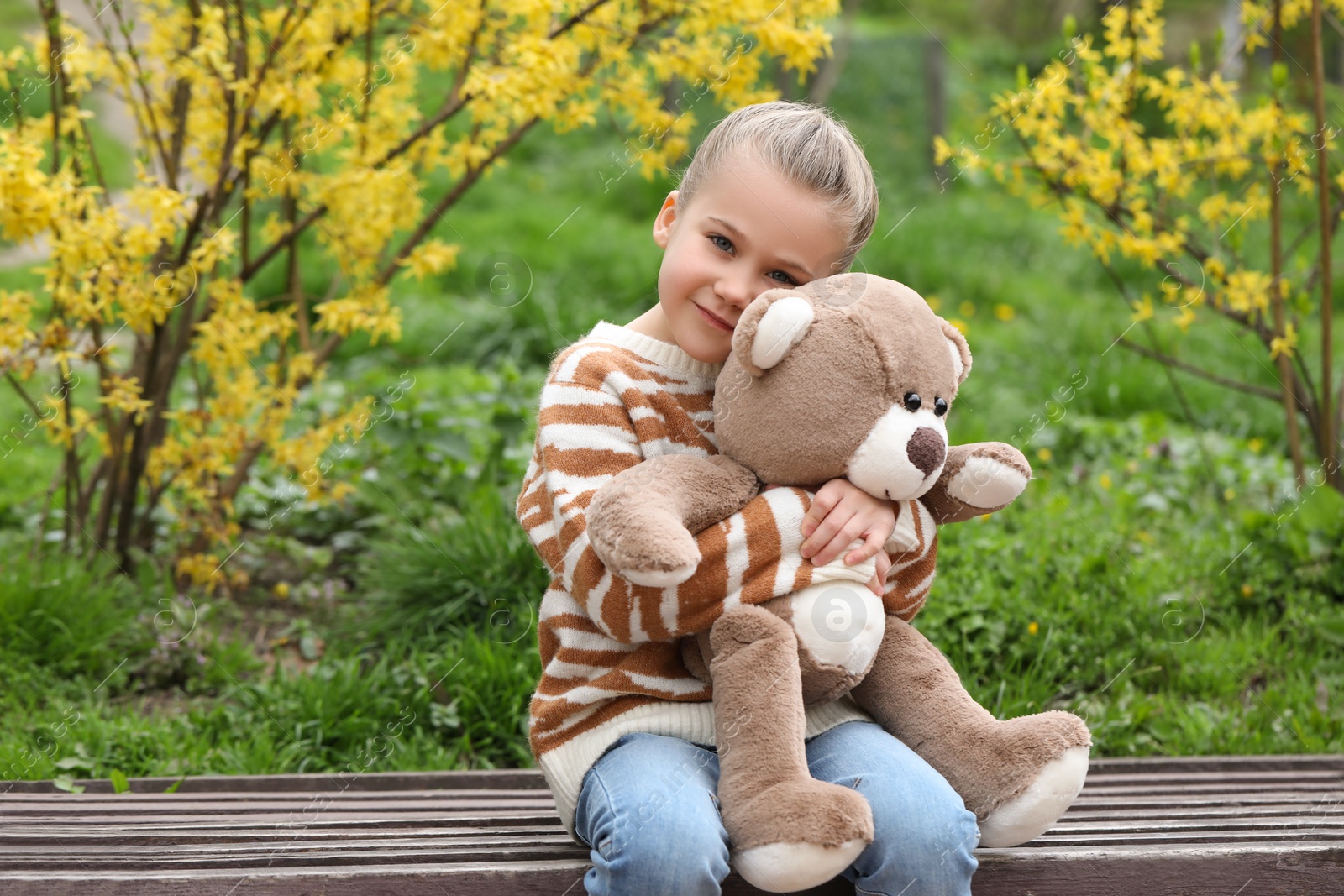 Photo of Little girl with teddy bear on wooden bench outdoors