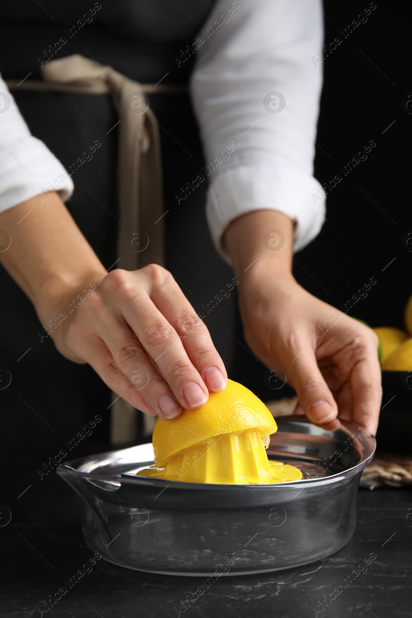 Photo of Woman squeezing lemon juice at black table, closeup