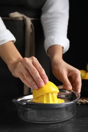 Woman squeezing lemon juice at black table, closeup