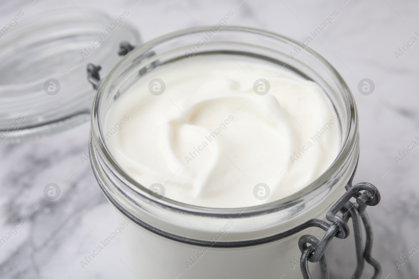 Photo of Delicious natural yogurt in glass jar on white marble table, closeup