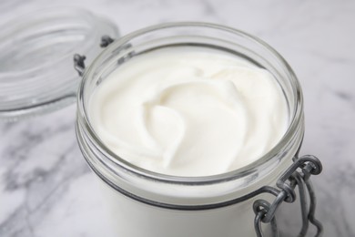 Photo of Delicious natural yogurt in glass jar on white marble table, closeup