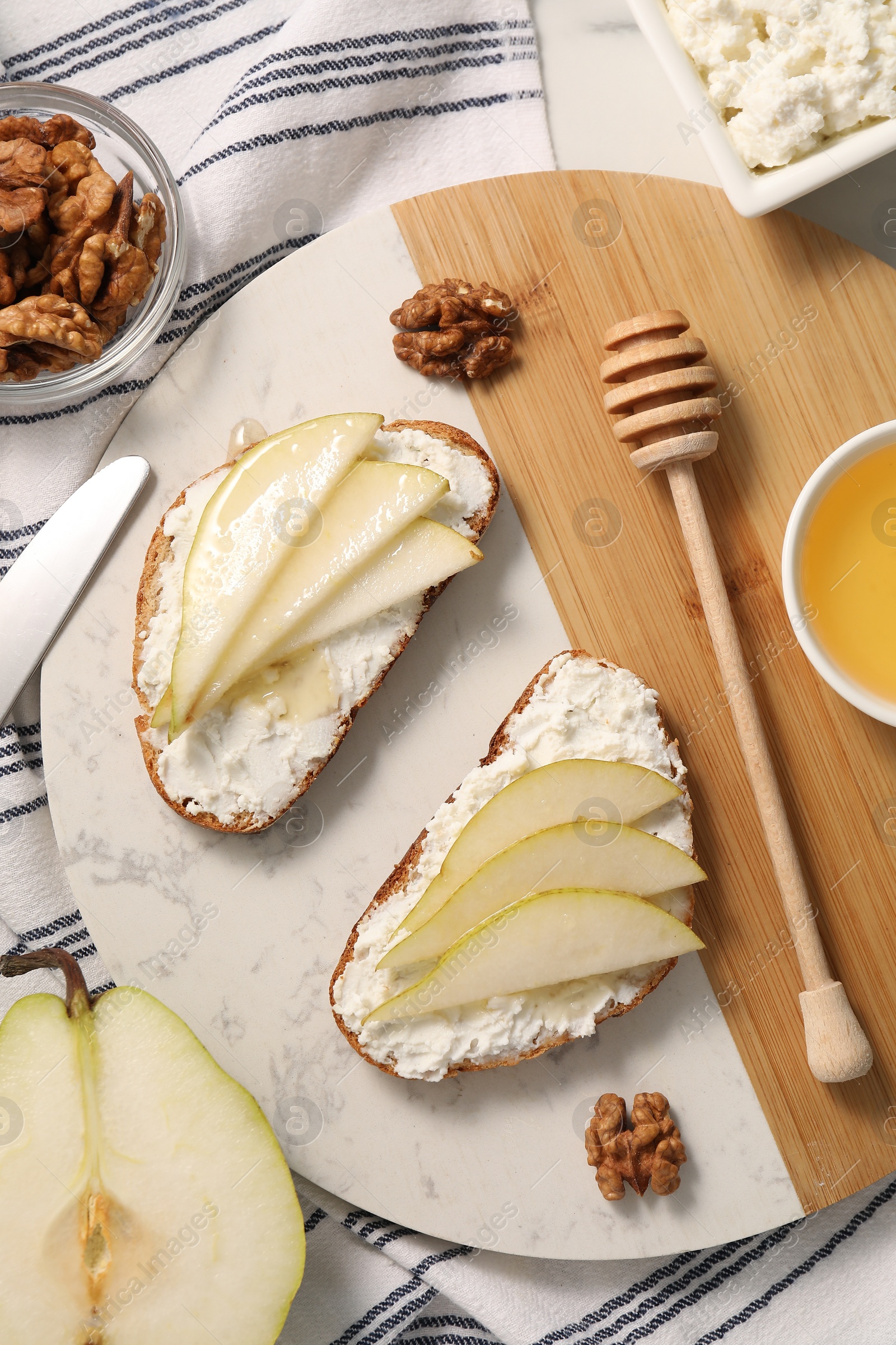 Photo of Delicious ricotta bruschettas with pear and walnut on white table, flat lay