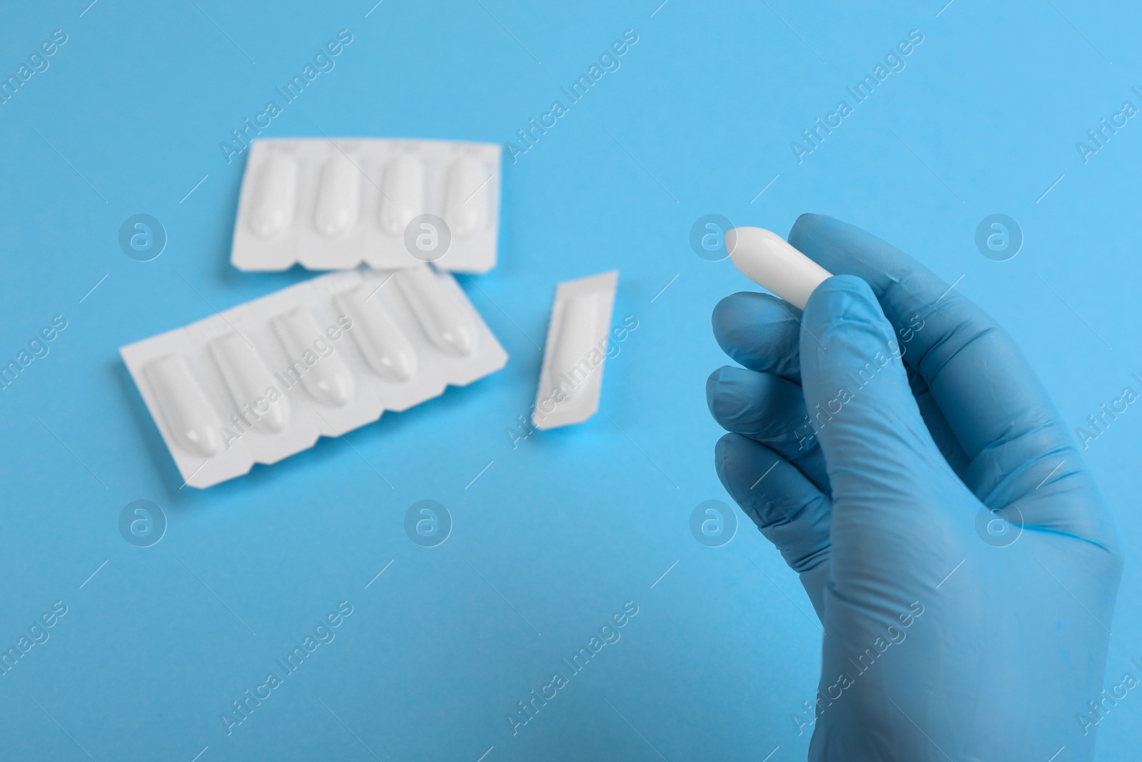 Photo of Woman holding suppository on light blue background, closeup. Hemorrhoid treatment