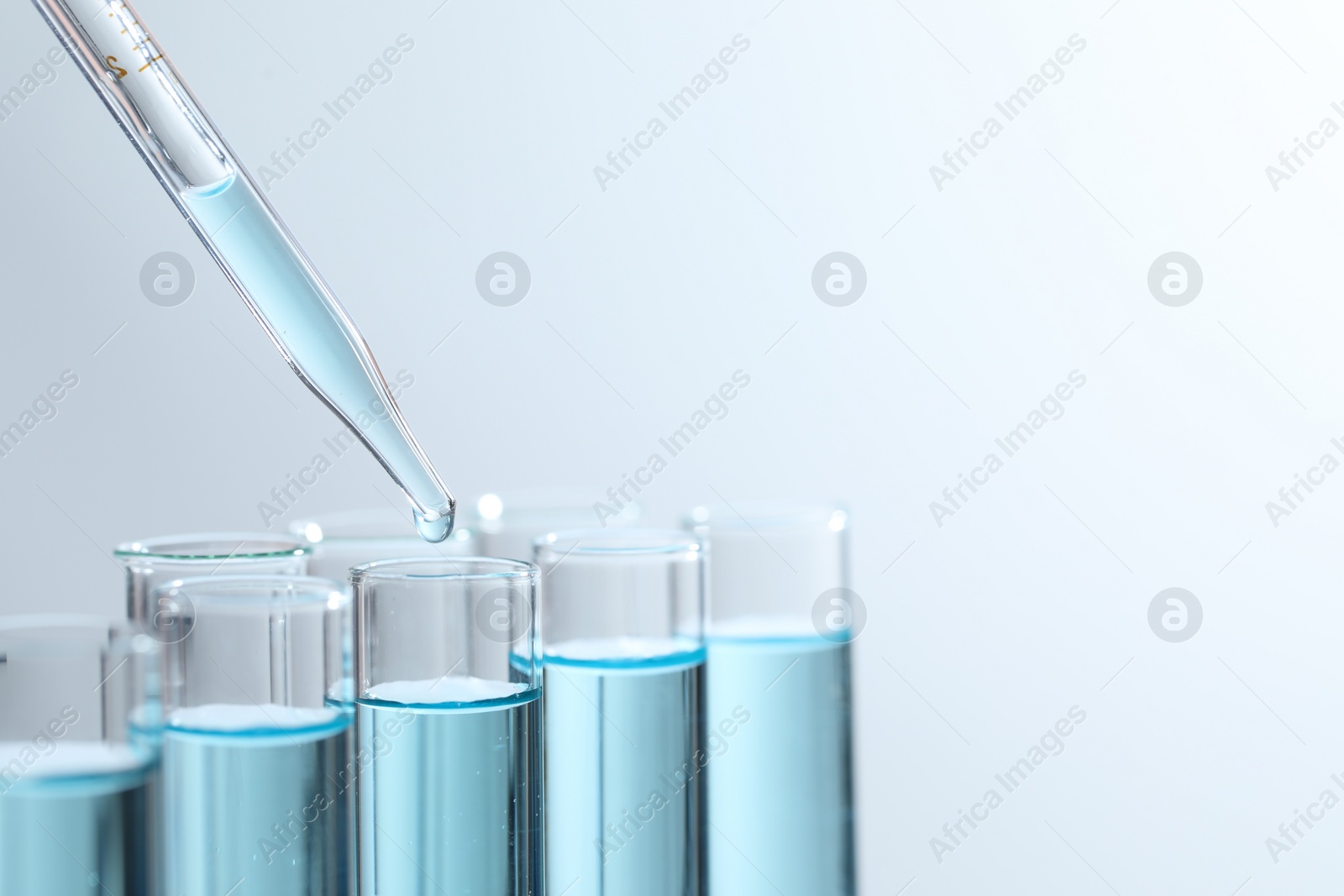 Photo of Dripping liquid from pipette into test tube on light background, closeup. Space for text