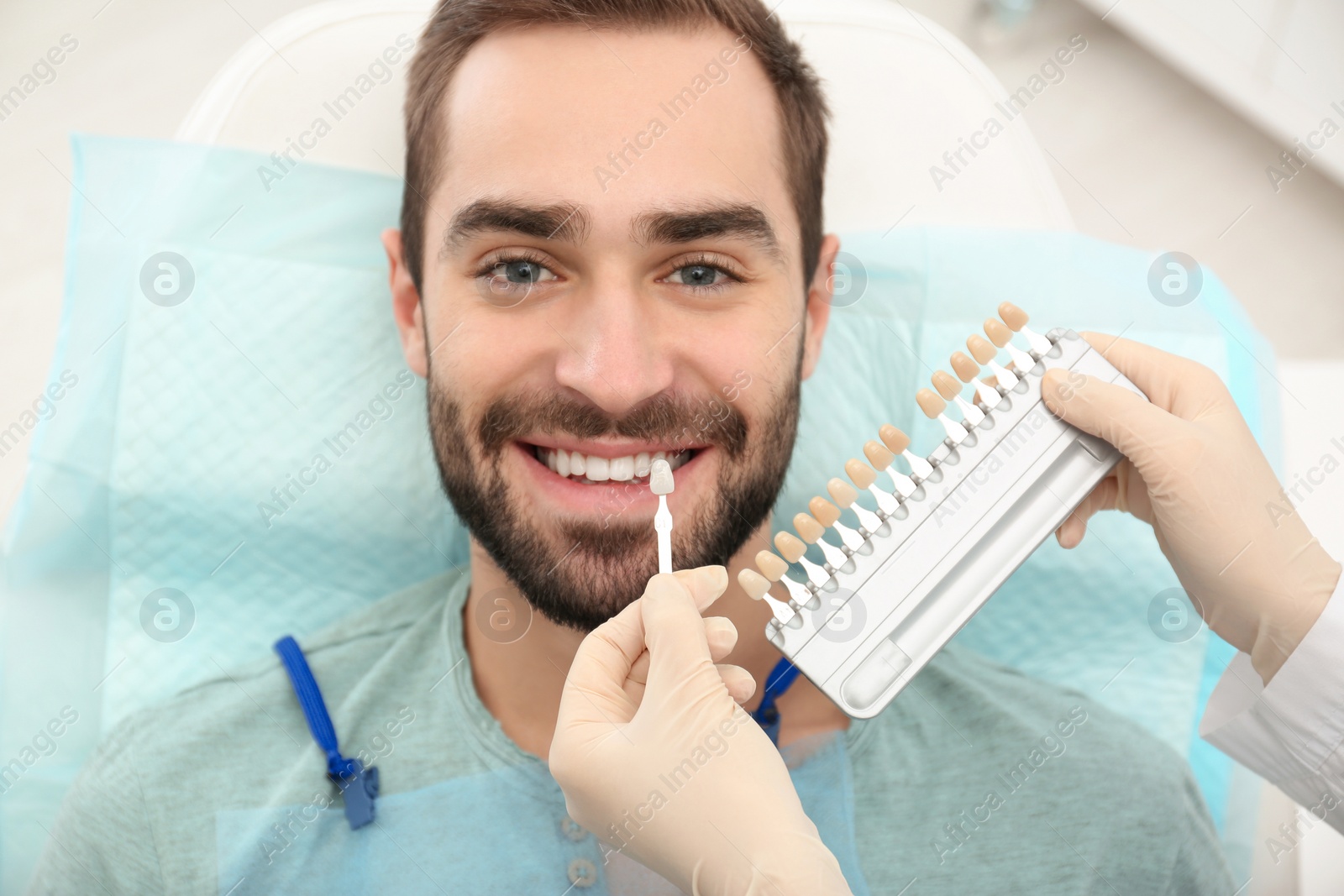 Photo of Dentist matching young man's teeth color with palette in office