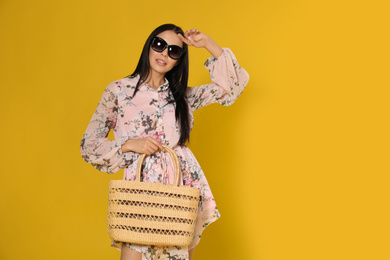 Young woman wearing floral print dress with straw bag on yellow background