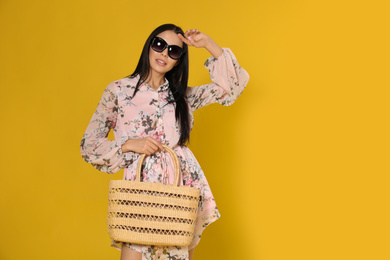 Photo of Young woman wearing floral print dress with straw bag on yellow background