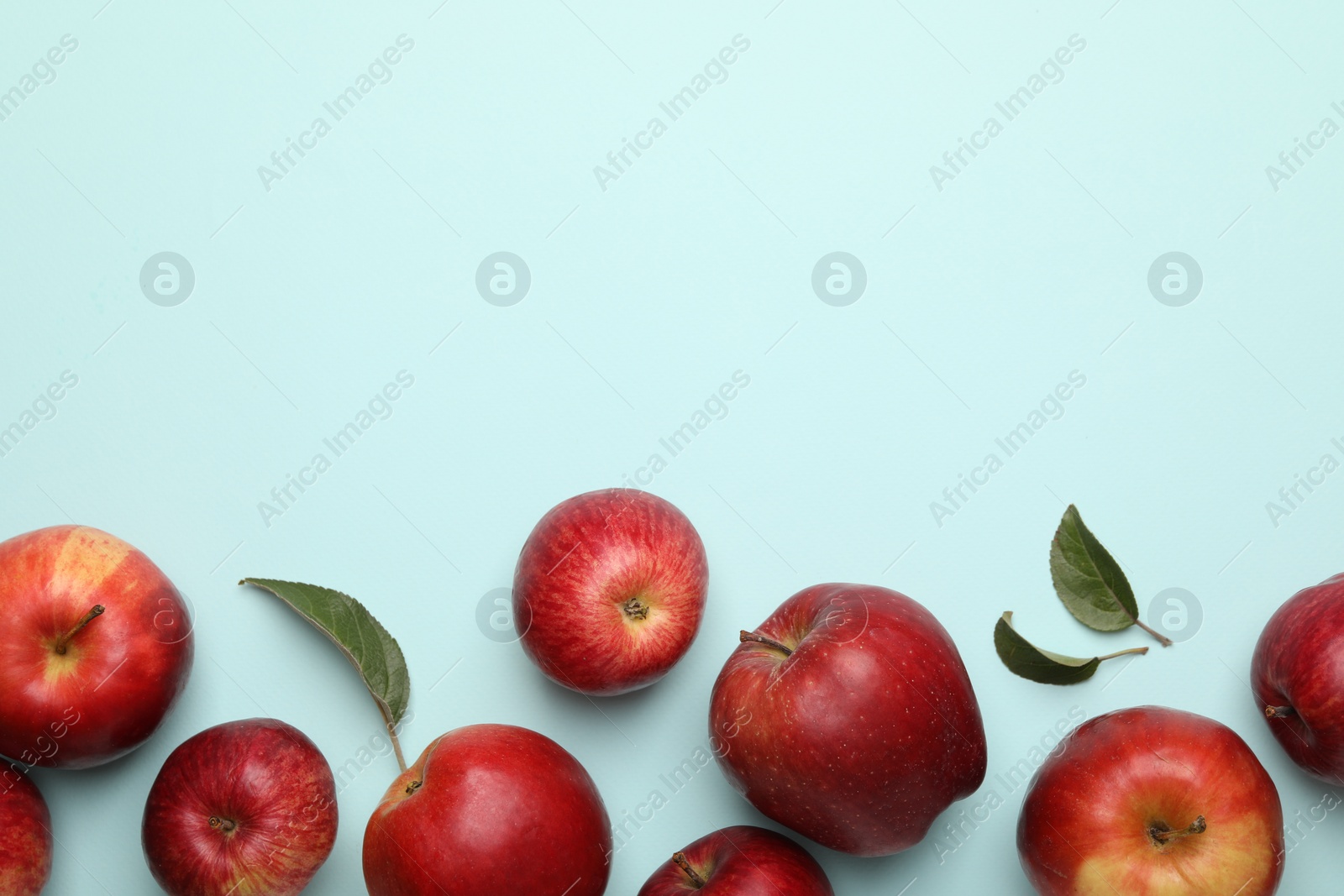 Photo of Fresh red apples and leaves on light blue background, flat lay. Space for text