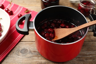 Pot with cherries in sugar syrup on wooden table. Making delicious jam