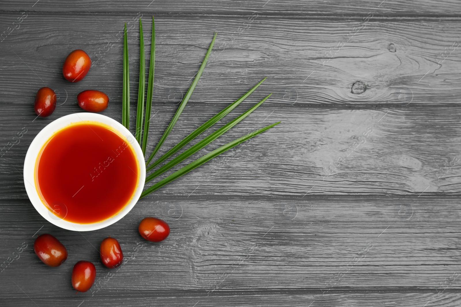 Photo of Palm oil in bowl, tropical leaf and fruits on grey wooden table. Space for text