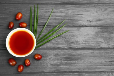 Palm oil in bowl, tropical leaf and fruits on grey wooden table. Space for text