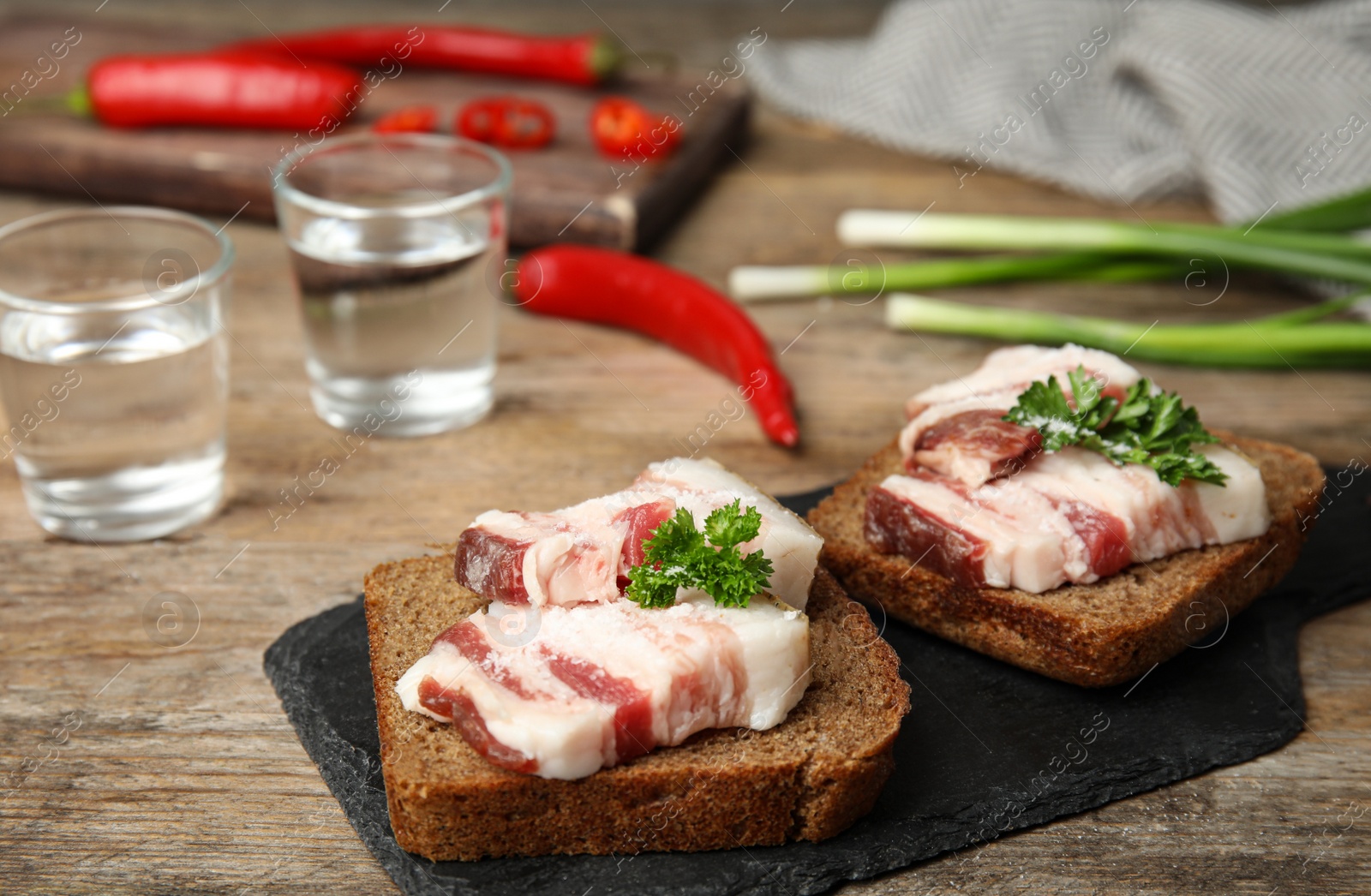 Photo of Board with pork fatback sandwiches, shots of vodka, onion and pepper on wooden table