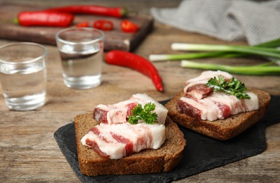 Board with pork fatback sandwiches, shots of vodka, onion and pepper on wooden table