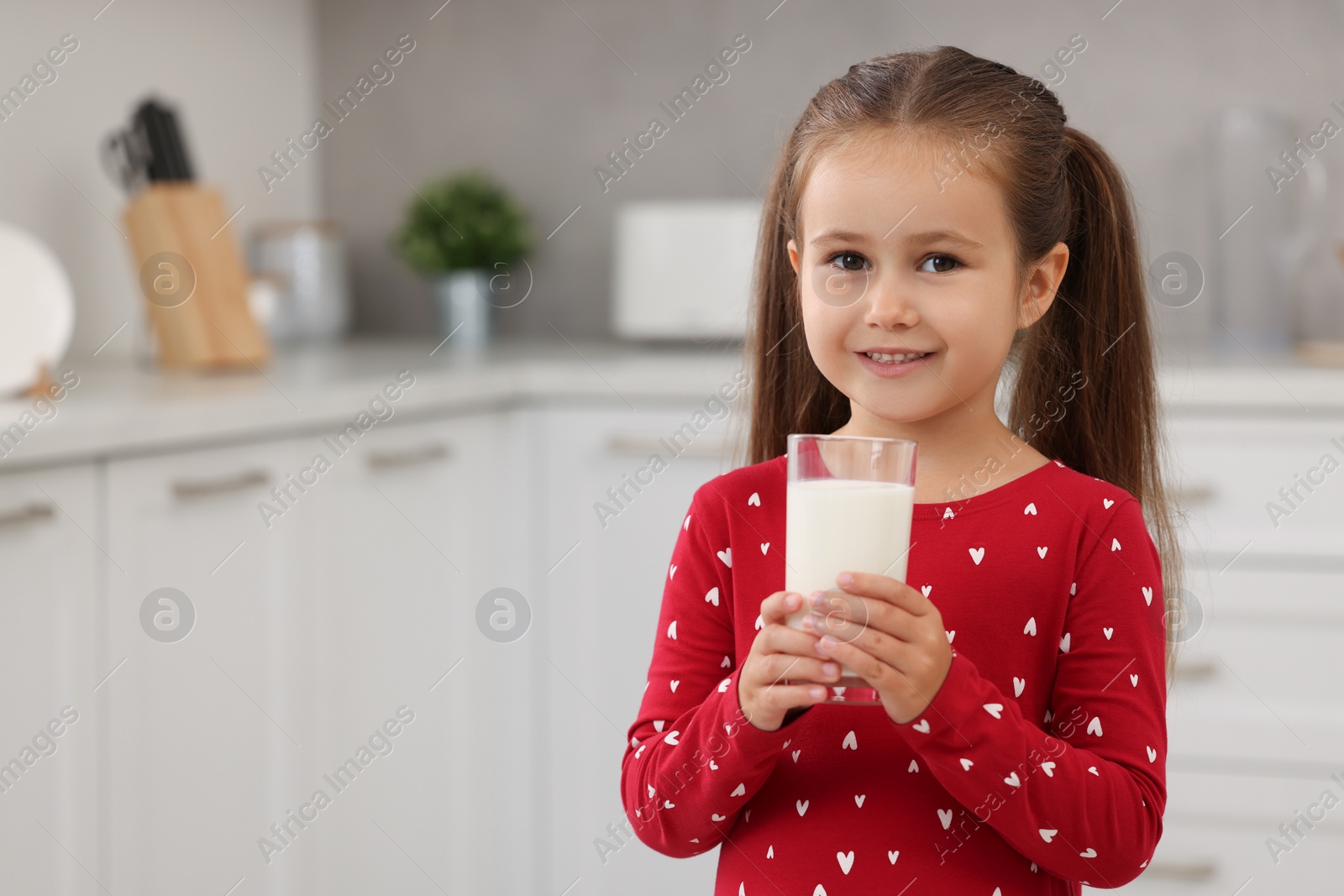 Photo of Cute girl with glass of fresh milk in kitchen, space for text