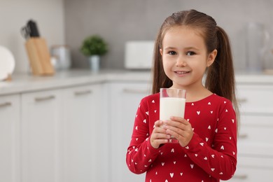 Photo of Cute girl with glass of fresh milk in kitchen, space for text