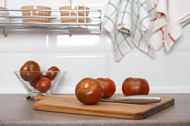 Photo of Wooden board with knife and tomatoes on kitchen table