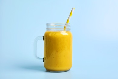 Mason jar with delicious fruit smoothie on light blue background