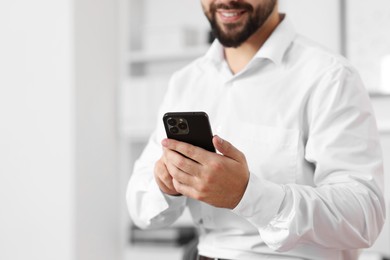 Young man using smartphone in office, closeup. Space for text