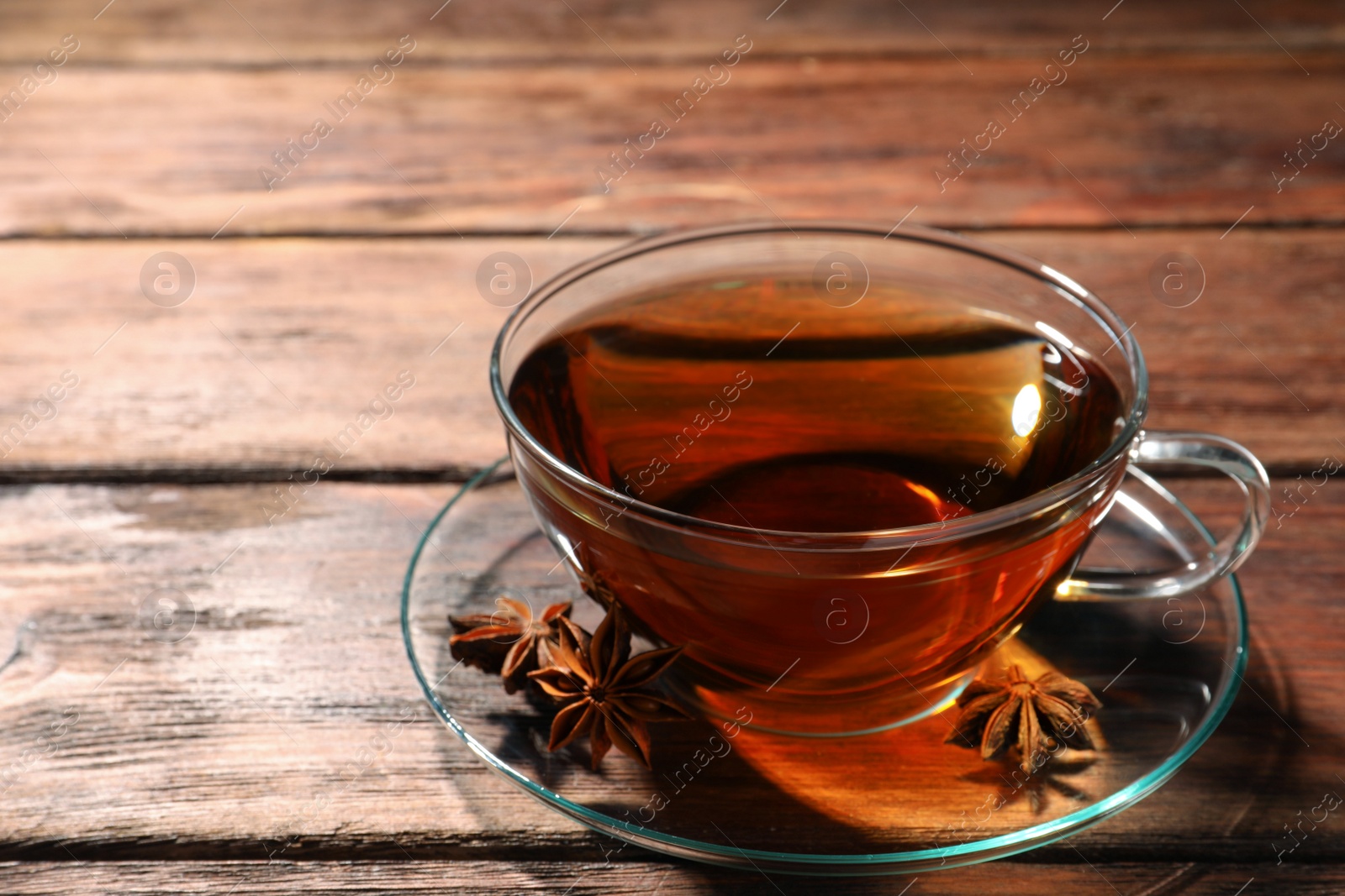 Photo of Glass cup of aromatic tea with anise stars on wooden table. Space for text