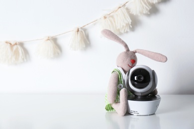 Photo of Modern CCTV security camera, toy bunny near wall with nursery garland. Space for text