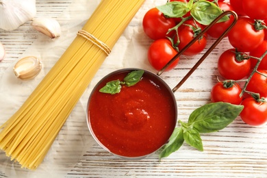 Photo of Flat lay composition with pan of sauce, pasta and tomatoes on wooden table
