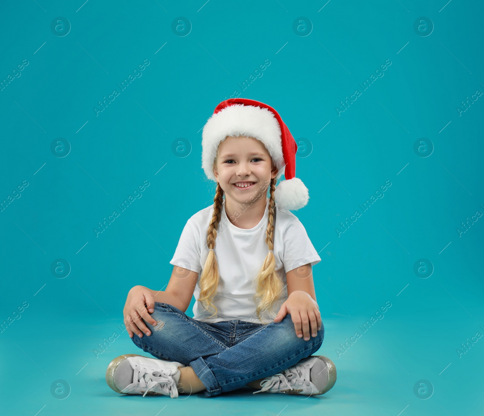 Photo of Cute little child wearing Santa hat on blue background. Christmas holiday