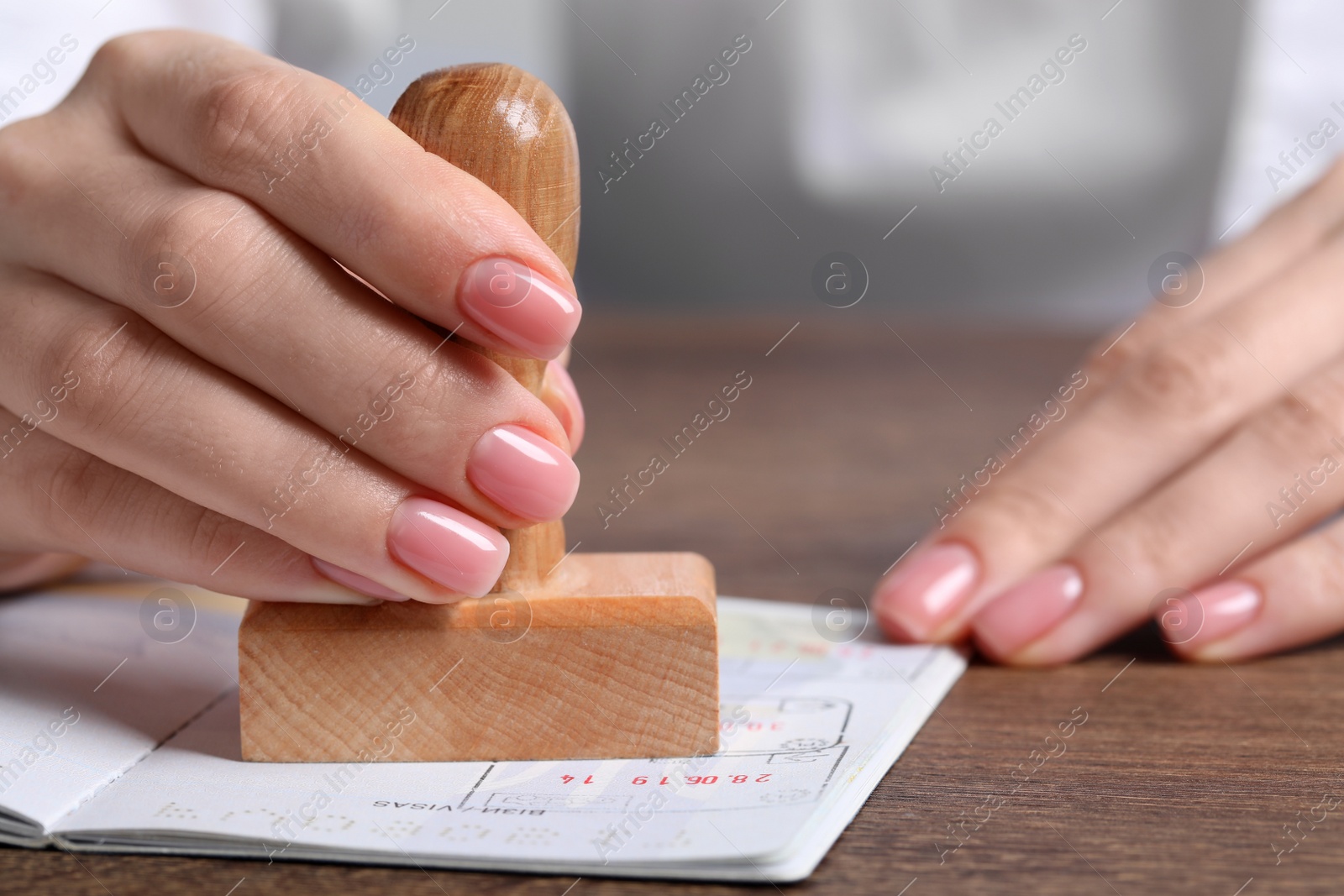 Photo of Ukraine, Lviv - September 6, 2022: Woman stamping visa page in passport at wooden table, closeup