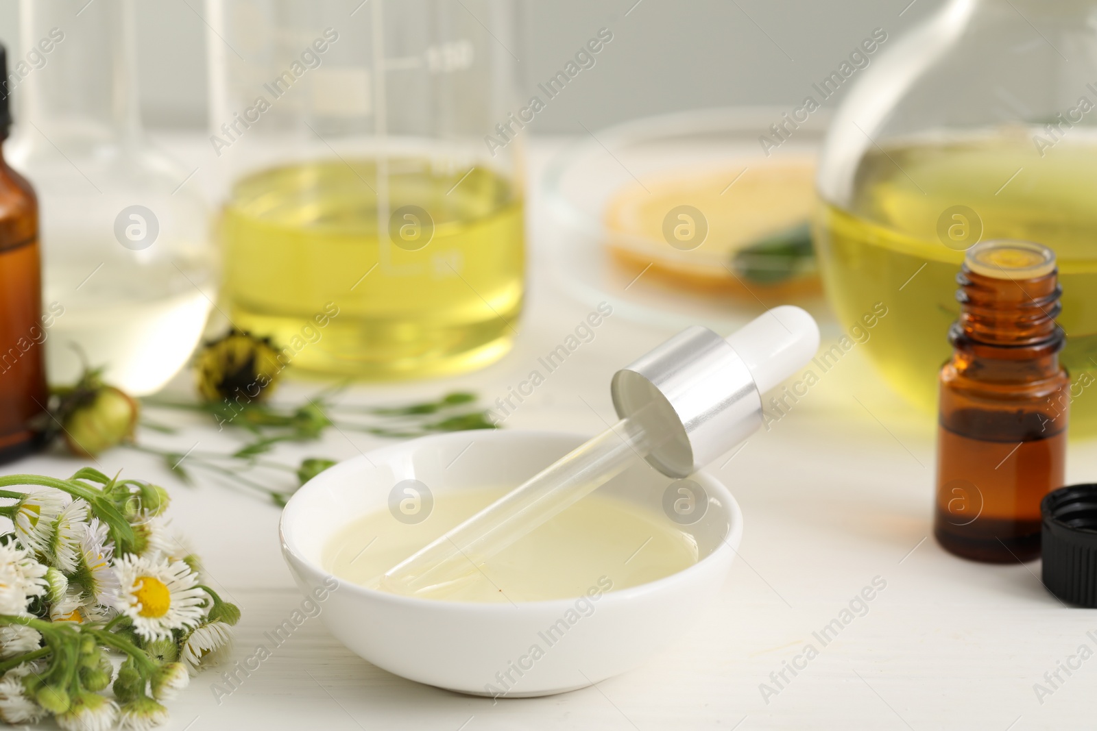 Photo of Cosmetic oil and dropper in bowl on white table, closeup