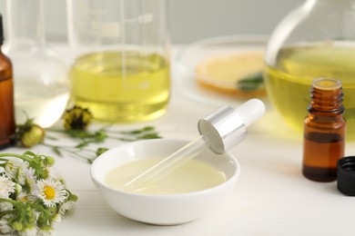 Photo of Cosmetic oil and dropper in bowl on white table, closeup