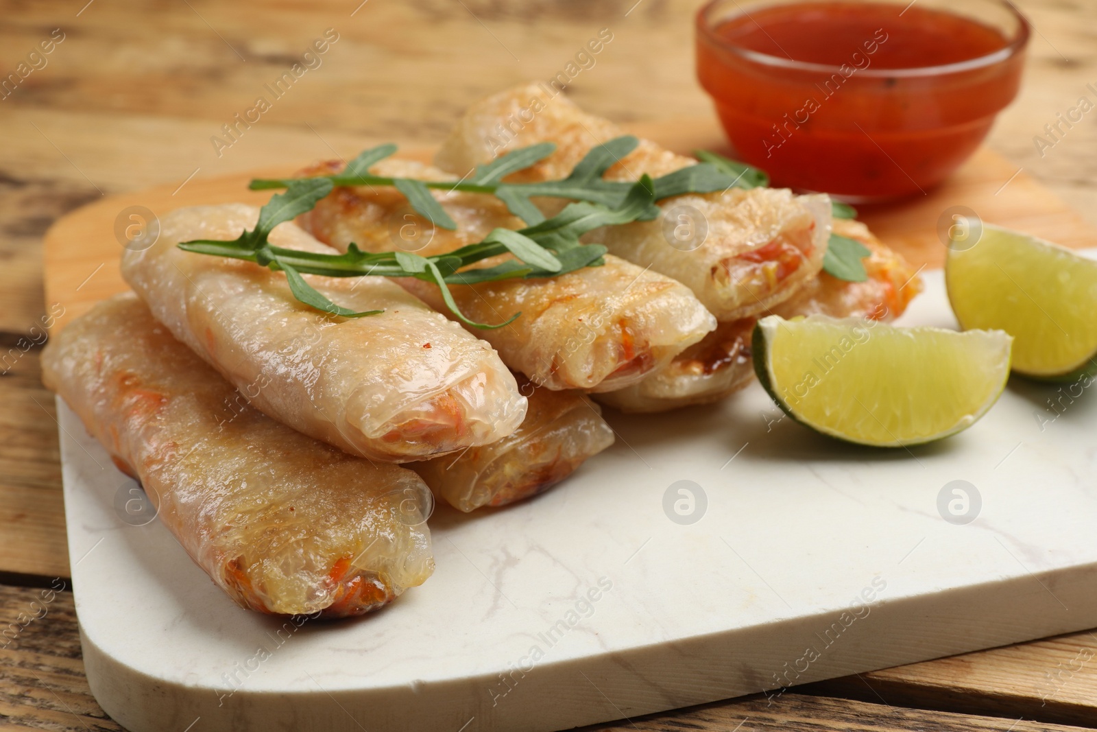 Photo of Tasty fried spring rolls, lime, arugula and sauce on wooden table, closeup