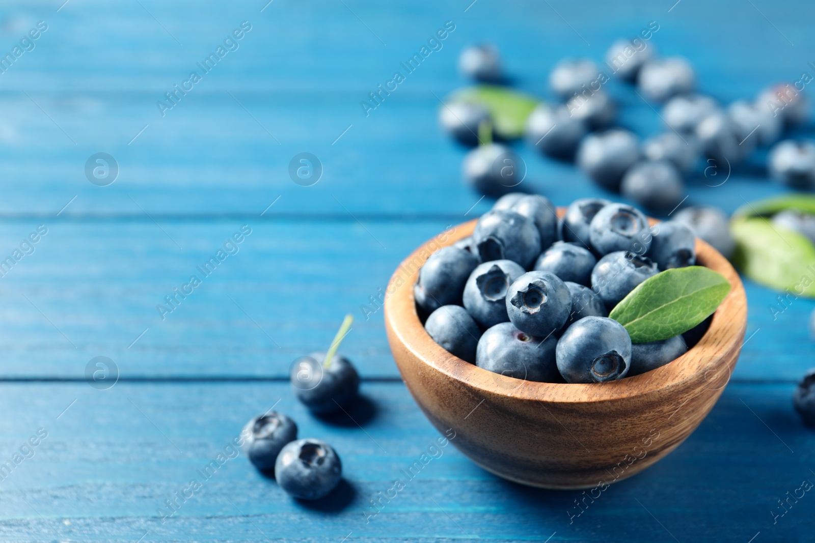 Photo of Bowl of fresh tasty blueberries on blue wooden table, closeup. Space for text