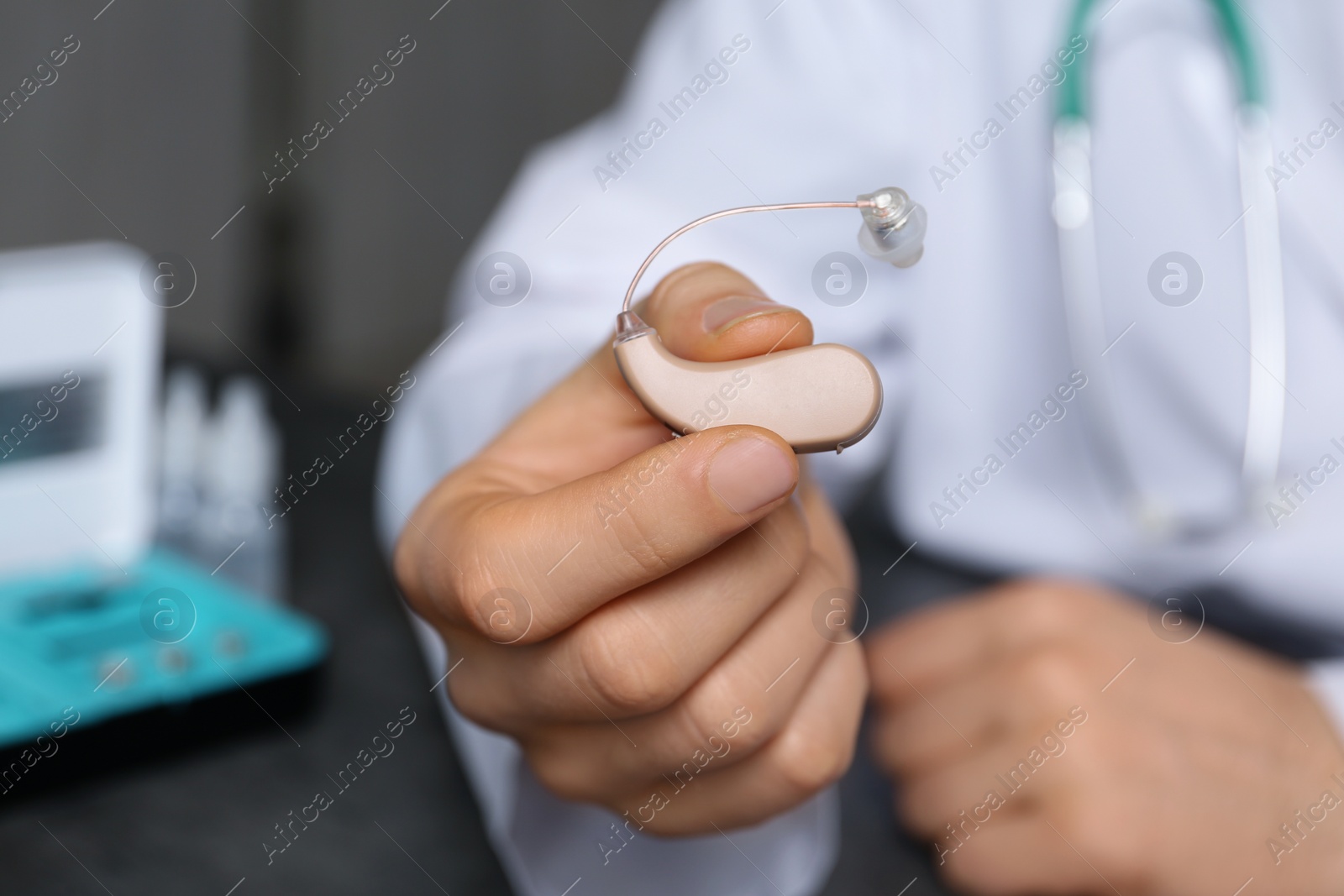 Photo of Doctor holding hearing aid against blurred background, closeup. Medical objects