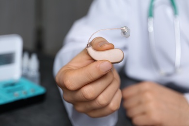 Photo of Doctor holding hearing aid against blurred background, closeup. Medical objects