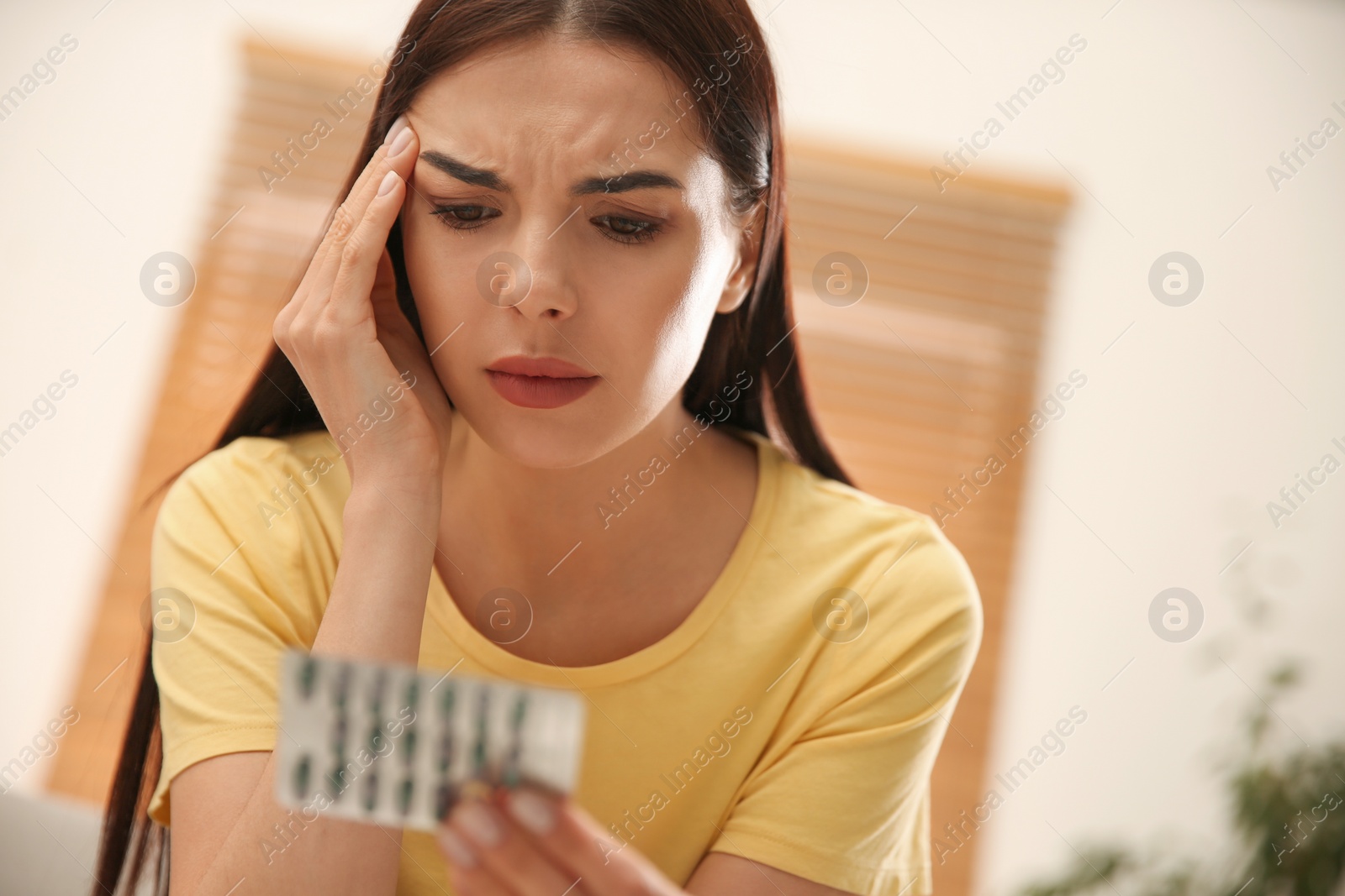 Photo of Confused young woman holding package of pills at home