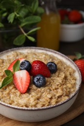 Photo of Tasty oatmeal with strawberries and blueberries in bowl on wooden table