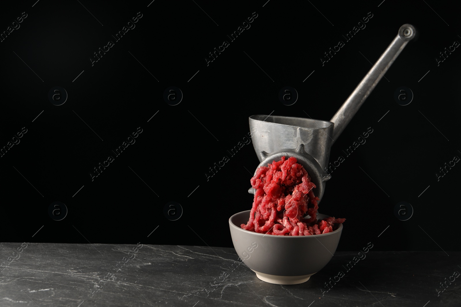 Photo of Metal meat grinder with beef mince on dark textured table against black background. Space for text