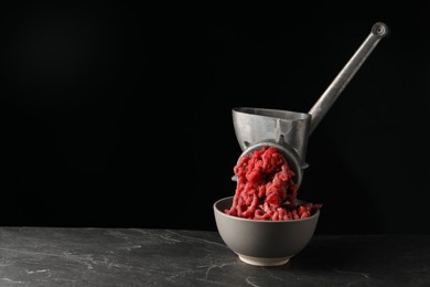 Metal meat grinder with beef mince on dark textured table against black background. Space for text