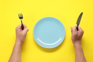 Photo of Man with fork, knife and empty plate at yellow table, top view