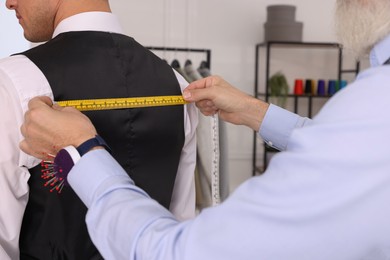 Photo of Professional tailor measuring client's back width in atelier, closeup