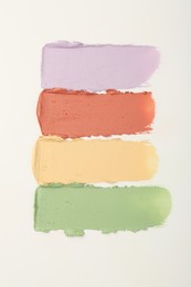 Samples of different color correcting concealers on white background, top view