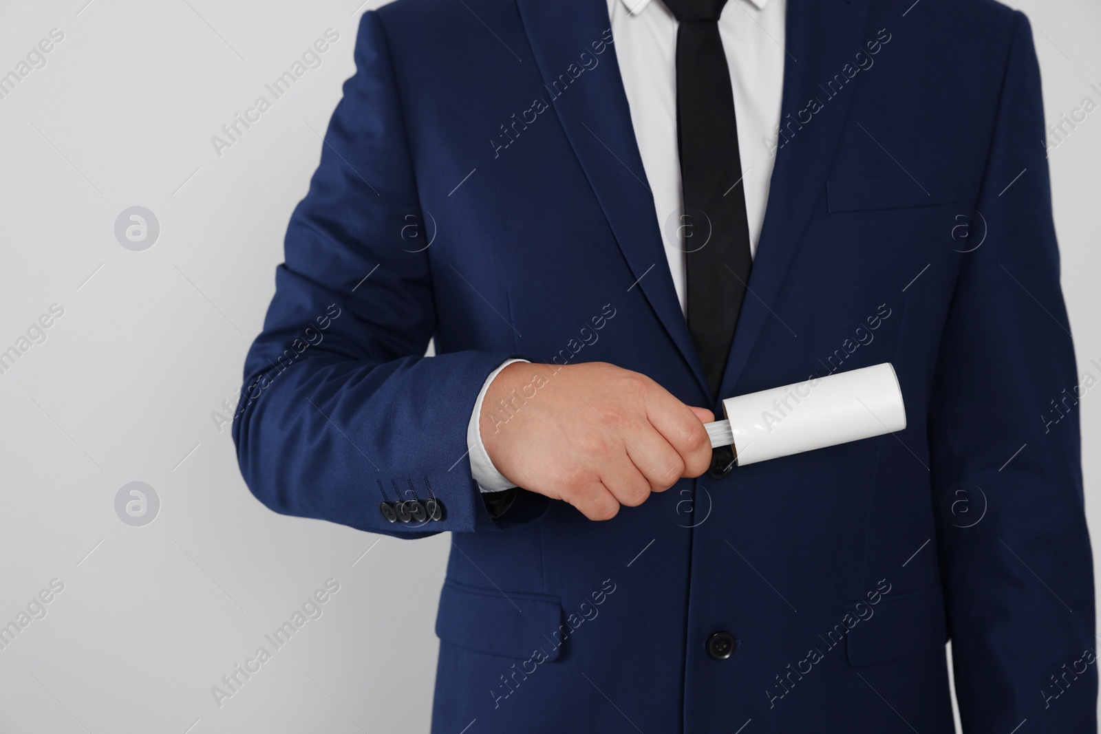 Photo of Man cleaning suit with lint roller on light grey background, closeup