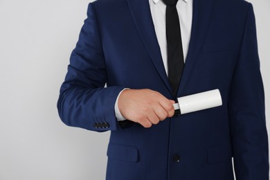 Photo of Man cleaning suit with lint roller on light grey background, closeup